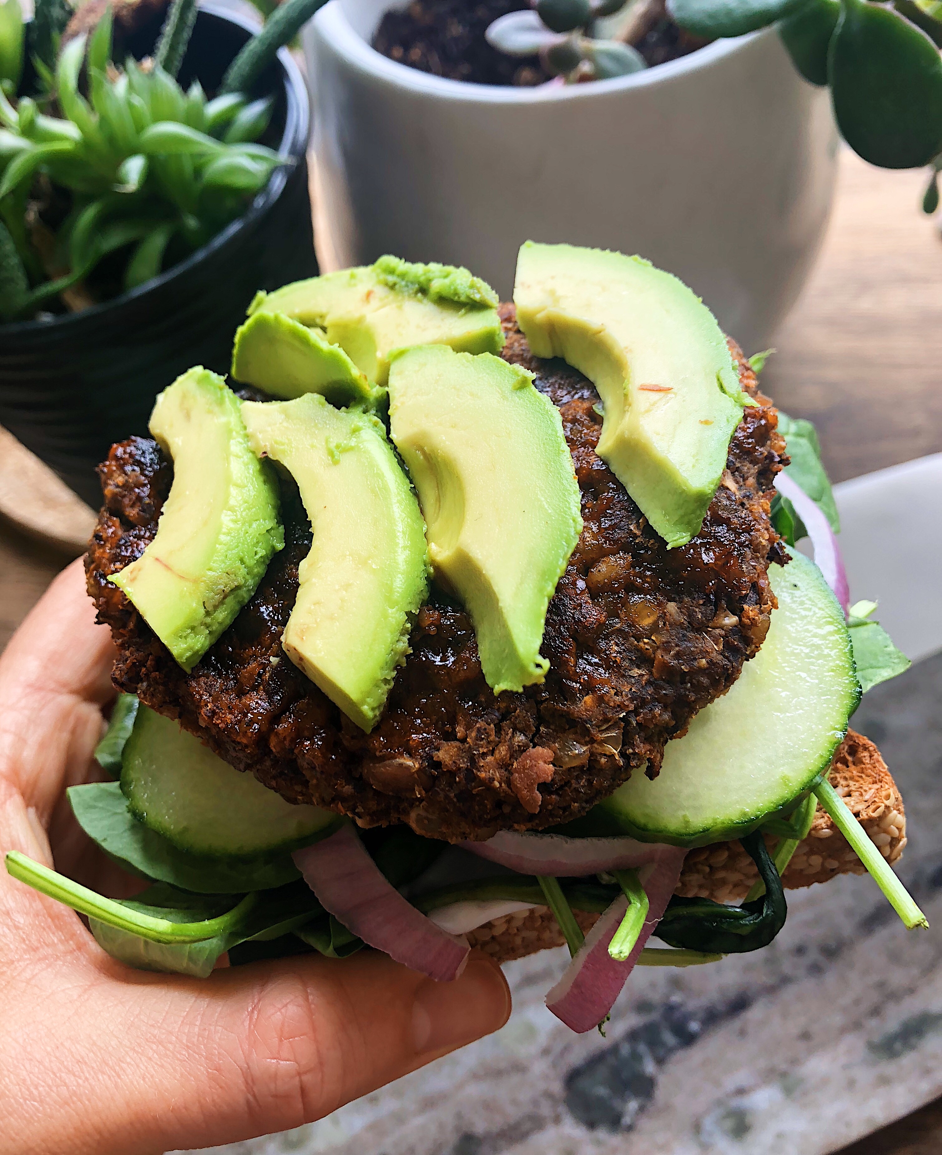 Hand holding veggie burger with avocado on top and a slice of bread.