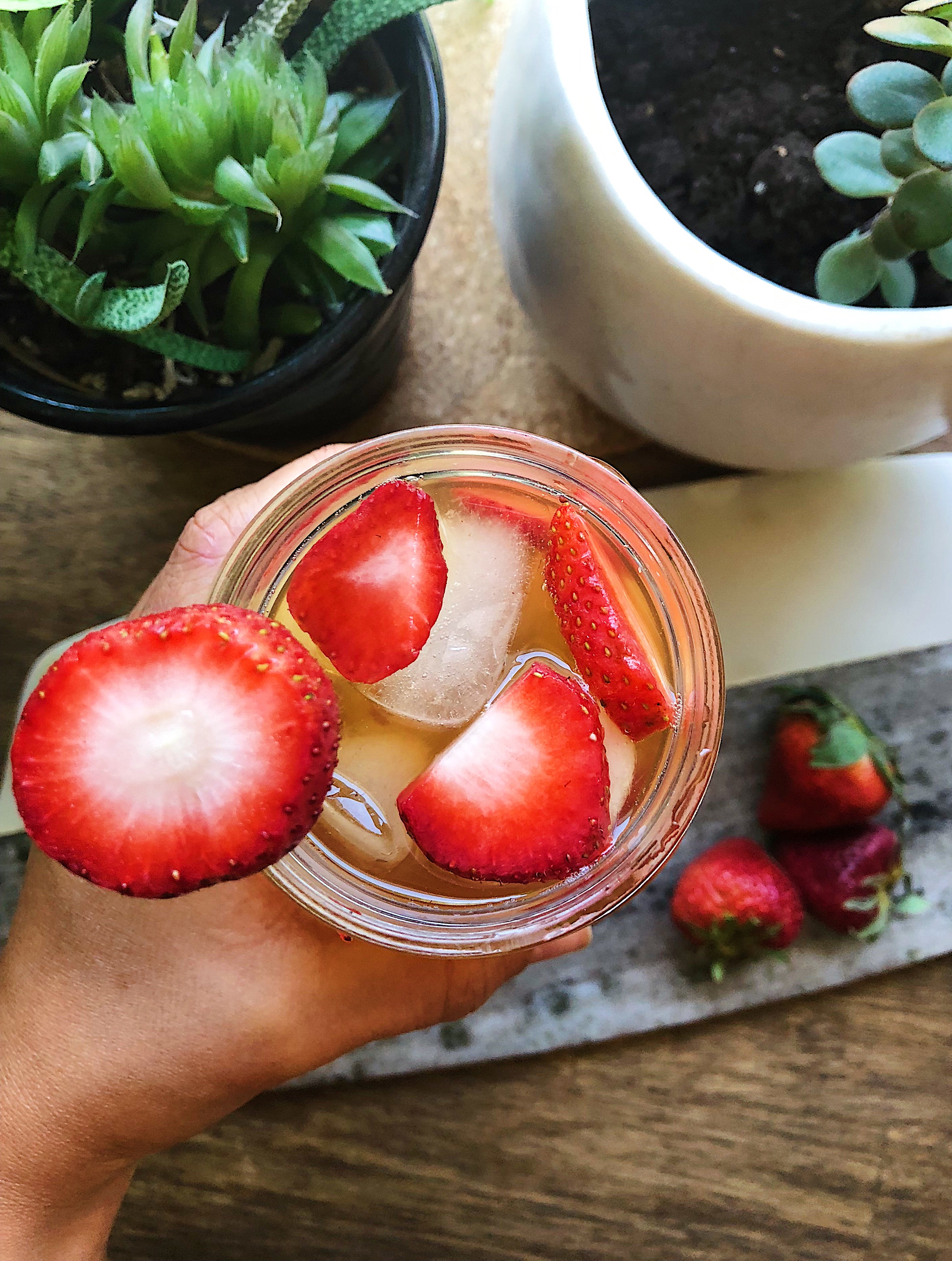 Hand holding a mason jar with kombucha and strawberries.