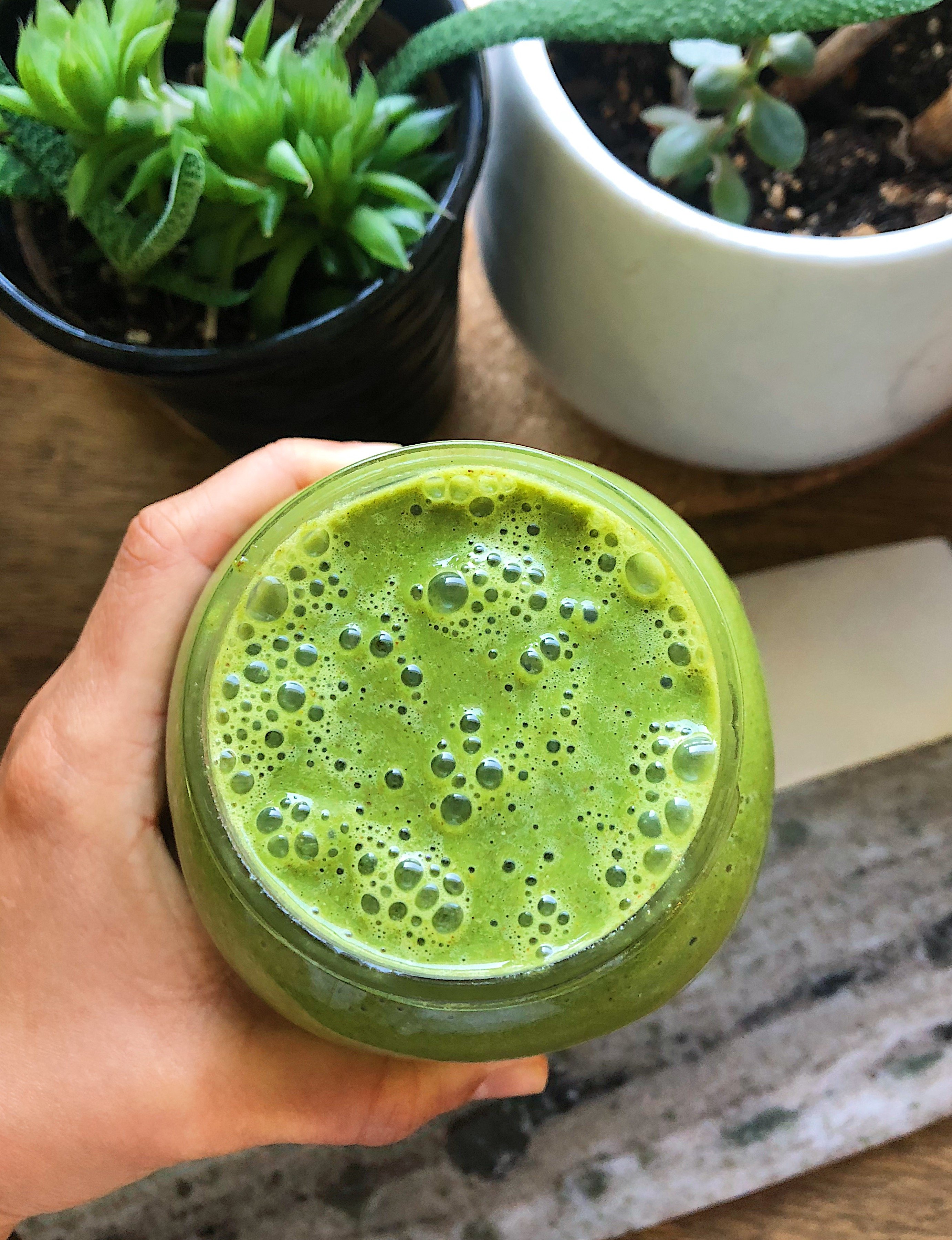 Hand holding green smoothie in a jar.