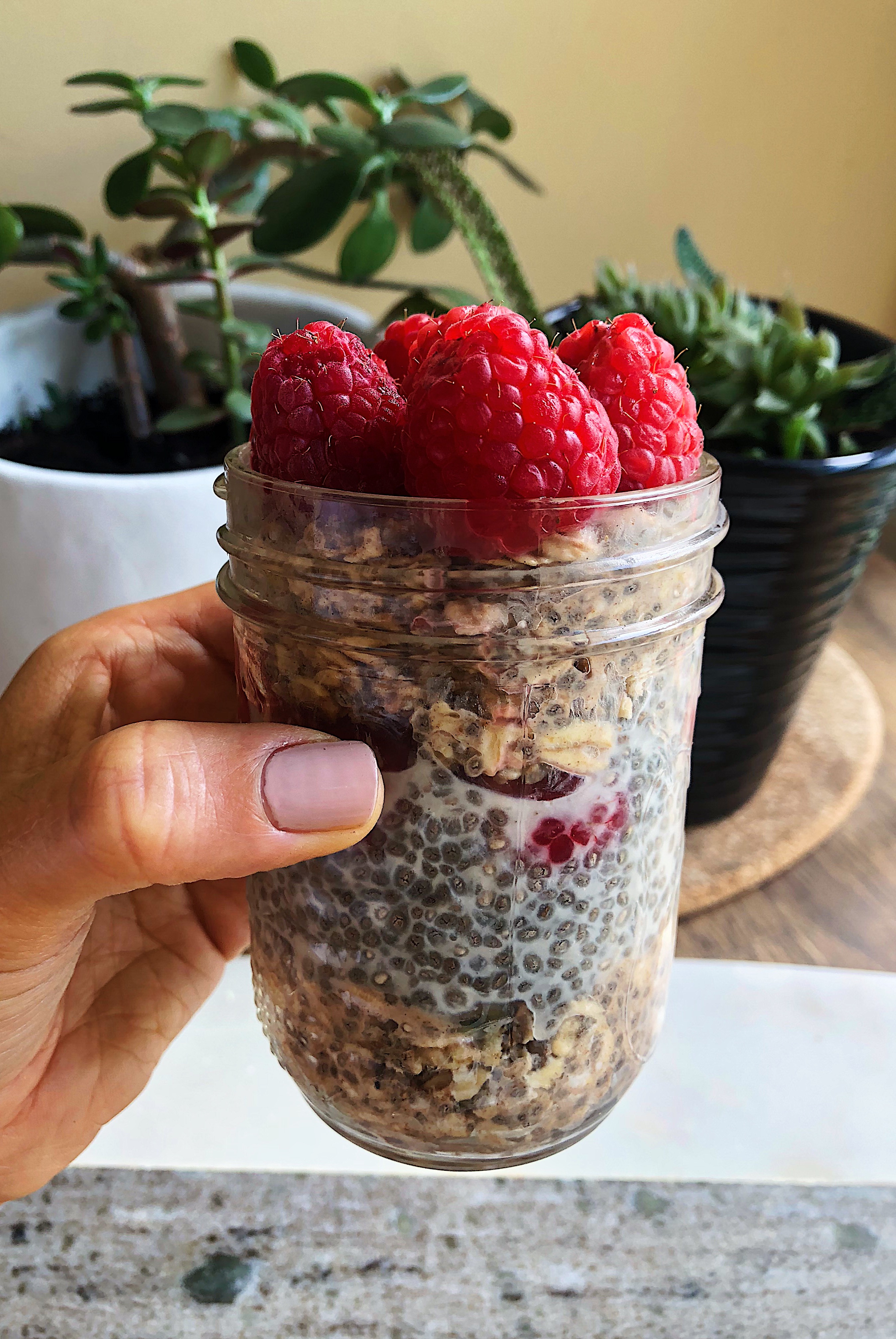 Hand holding jar of overnight oats with raspberries on top.