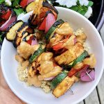 White bowl with veggie kabobs and tofu over quinoa with peanut lime sauce on top.