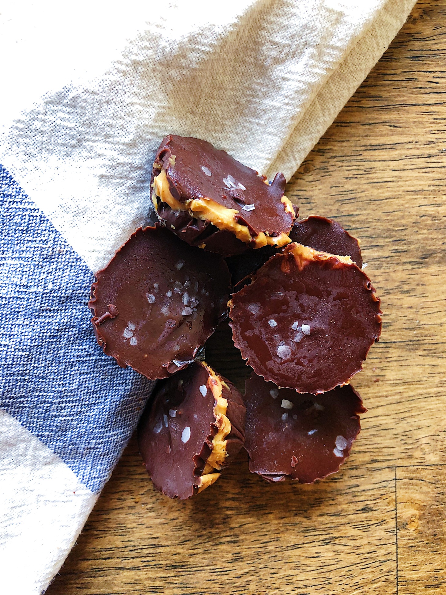 Homemade peanut butter cups on a wooden board with a napkin and flaky salt on top.