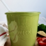 Jar with green smoothie with strawberries and spinach in the background.