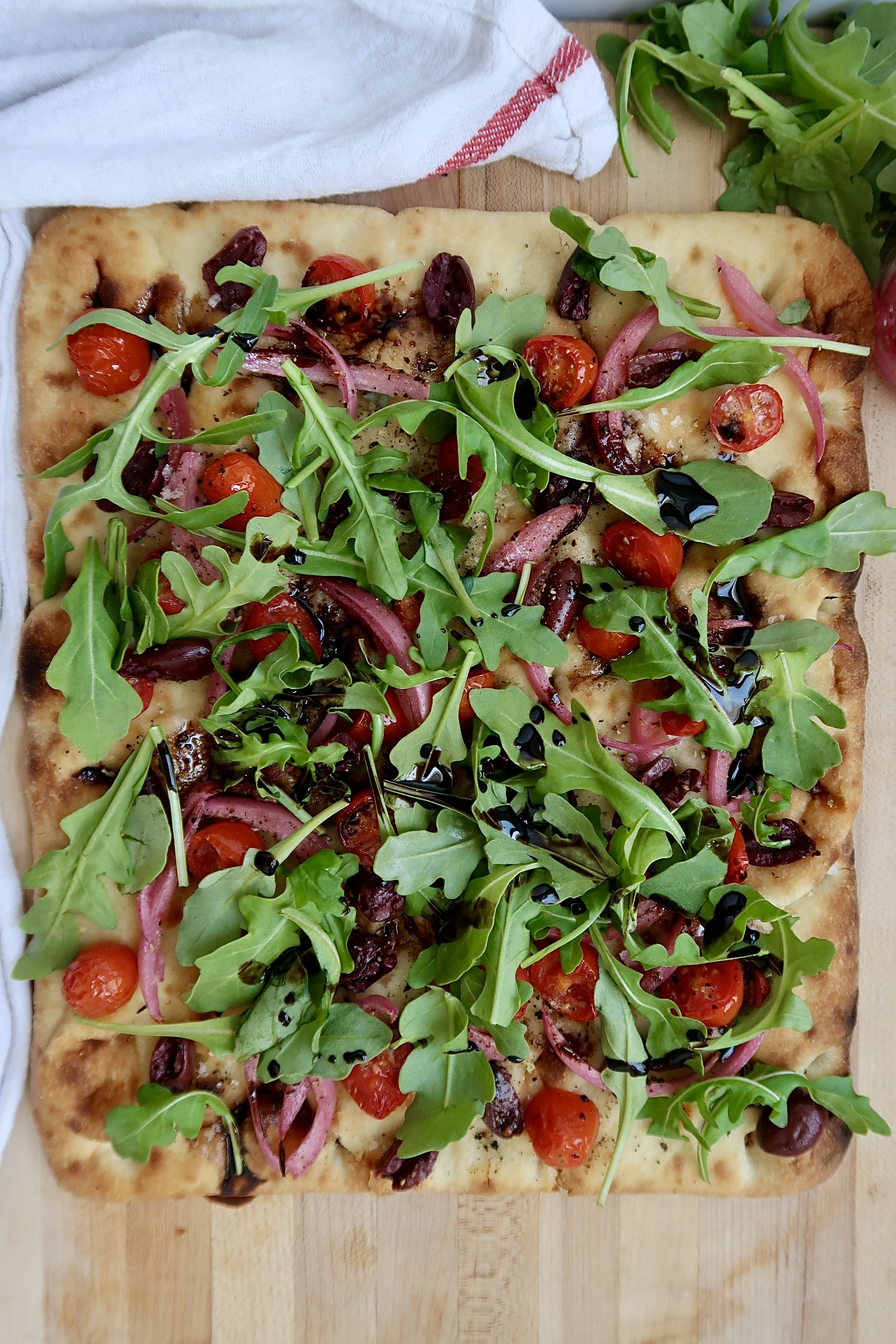 Flatbread with cherry tomato, olives and arugula and balsamic glaze