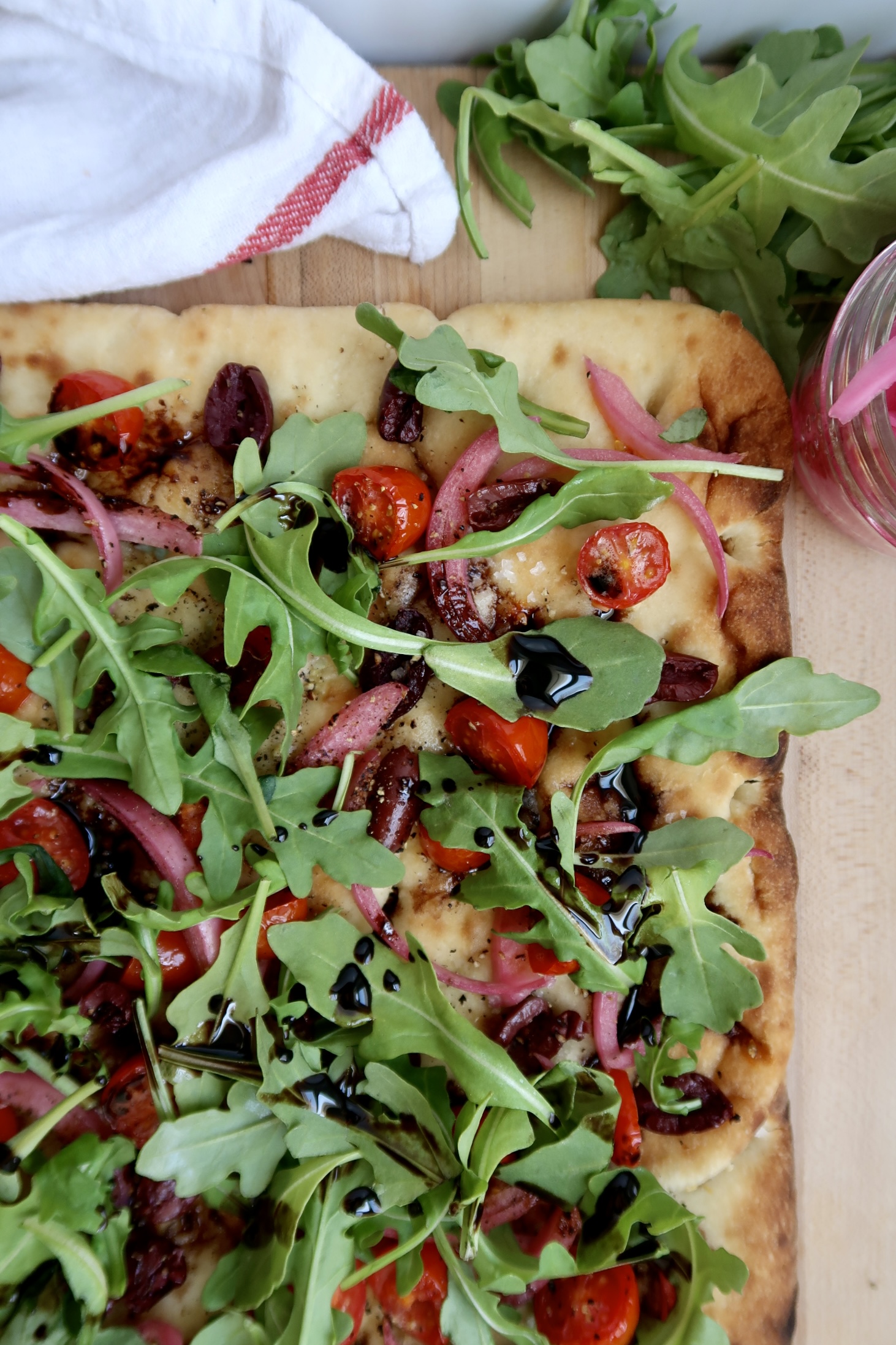 Flatbread with cherry tomato, olives and arugula and balsamic glaze