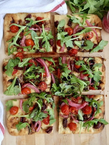 Flatbread with cherry tomato, olives and arugula and balsamic glaze, sliced.