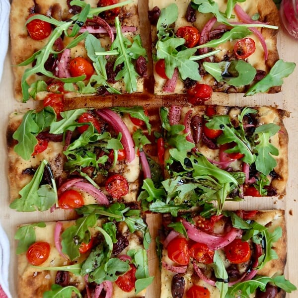 Flatbread with cherry tomato, olives and arugula and balsamic glaze, sliced.