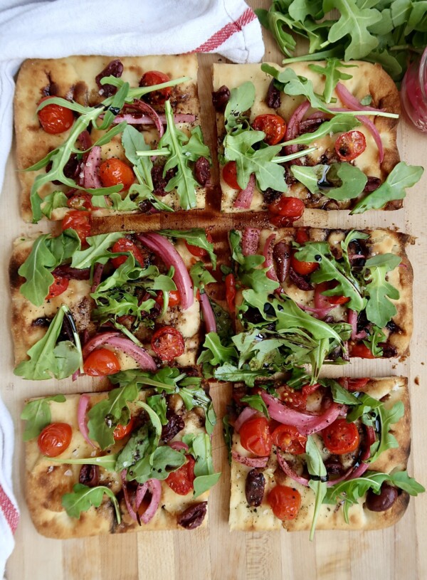Flatbread with cherry tomato, olives and arugula and balsamic glaze, sliced.