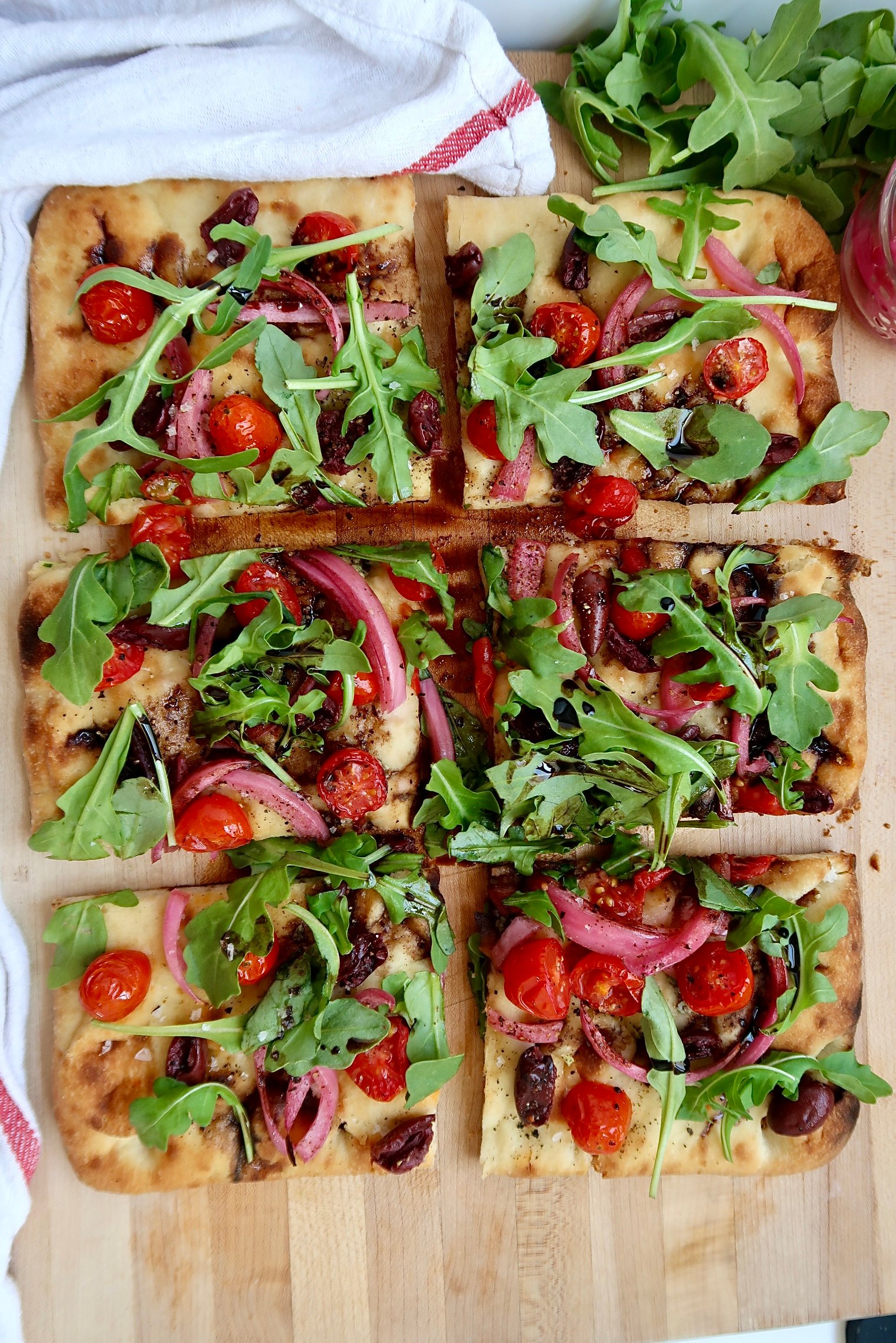 Flatbread with cherry tomato, olives and arugula and balsamic glaze, sliced.