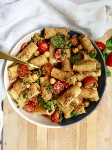 Bowl with pasta covered in sundried tomato pesto with cherry tomatoes, chickpeas and spinach and a fork with some on it.