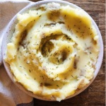 A bowl of mashed potatoes swirled with thyme and a blue and white napkin to the side.