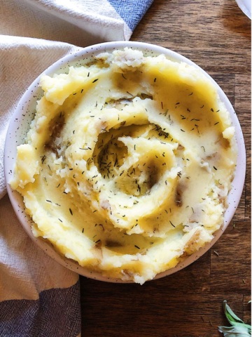 A bowl of mashed potatoes swirled with thyme and a blue and white napkin to the side.