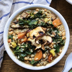 Bowl of soup with beans, rice, kale, carrots and mushrooms and a spoon to the side.