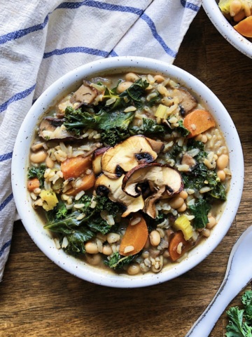 Bowl of soup with beans, rice, kale, carrots and mushrooms and a spoon to the side.