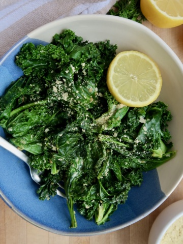 Bowl with wilted kale with nutritional yeast and a lemon.