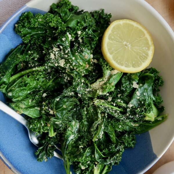 Bowl with wilted kale with nutritional yeast and a lemon.