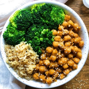Table with a white cloth and white bowl with sticky sesame chickpeas, steamed broccoli and rice.