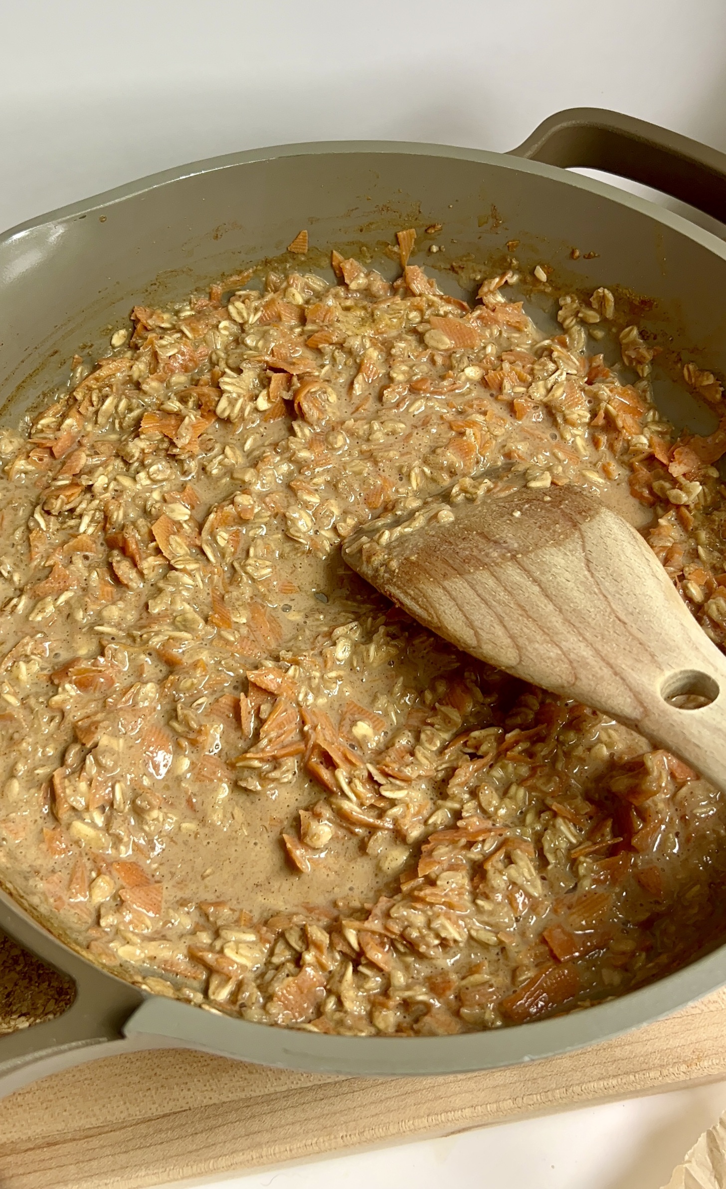 Pot with oatmeal cooking with carrot and a wooden spoon stirring it.