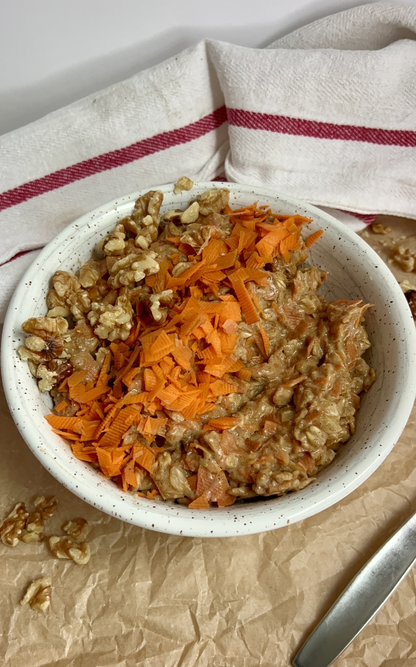 White bowl on parchment paper with oatmeal, grated carrot, and walnuts on top.