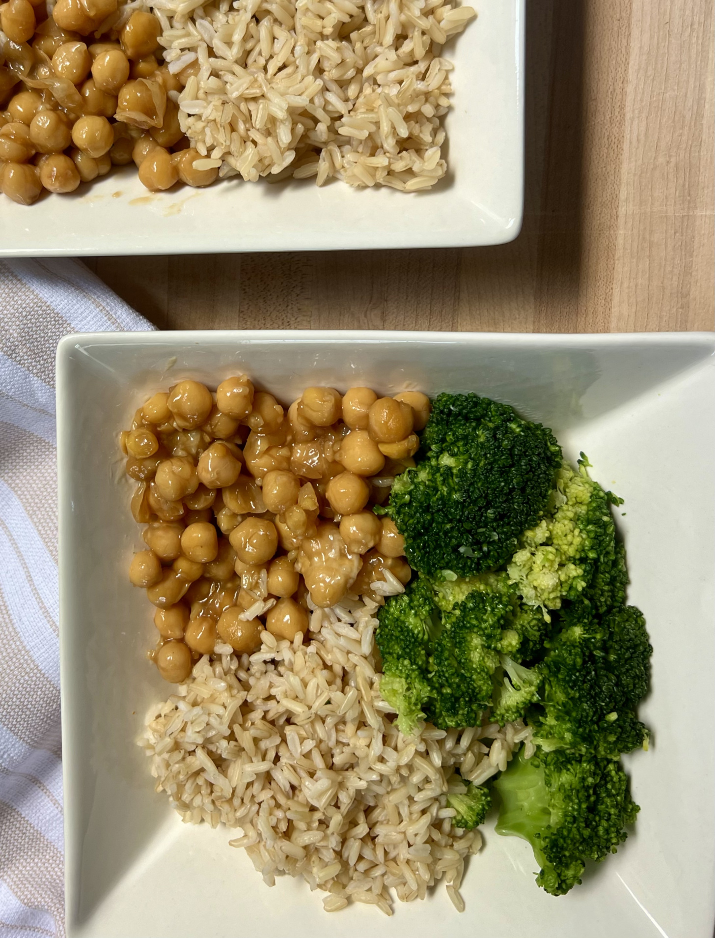 Two white bowls with sauce coated chickpeas, broccoli and brown rice