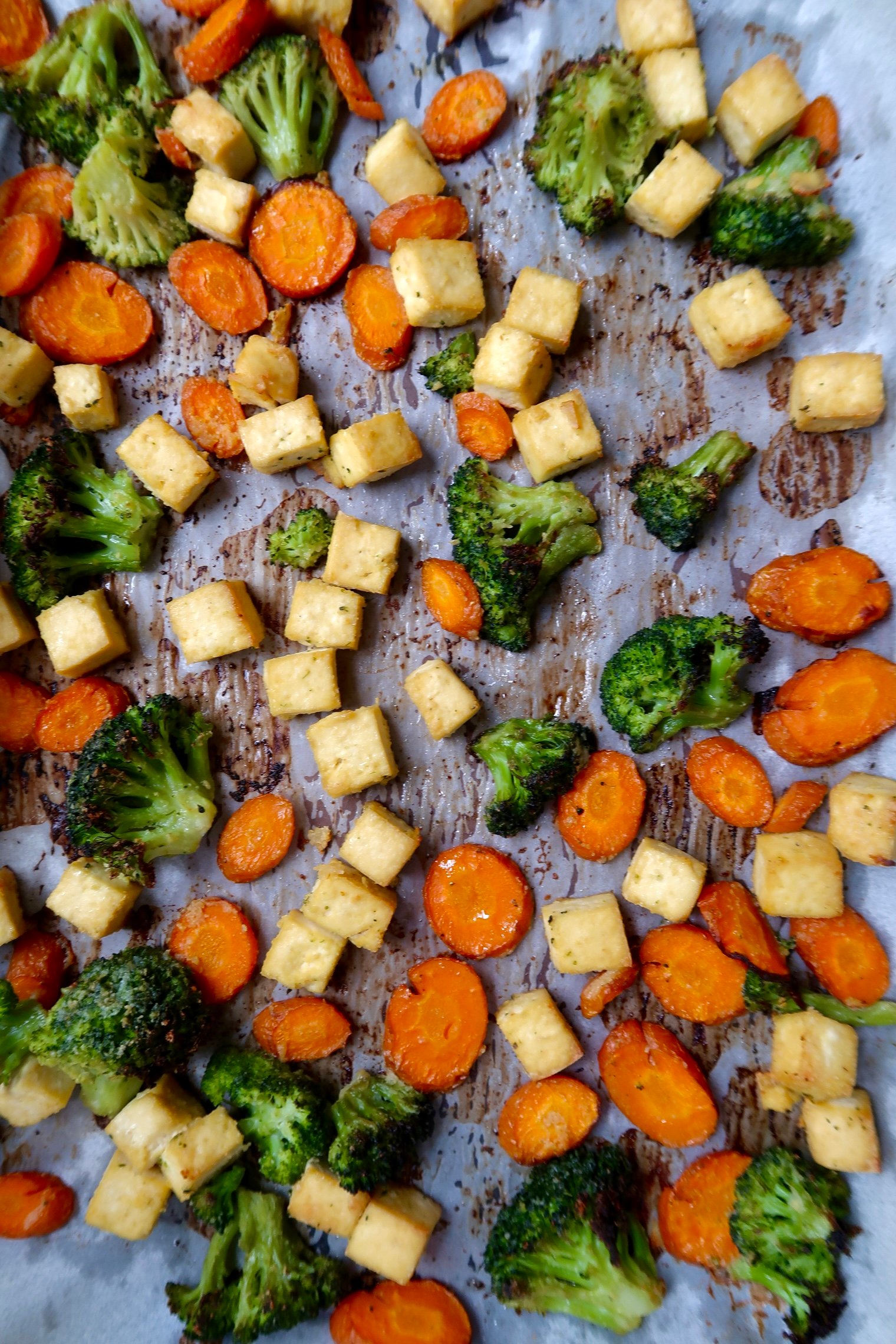 Sheet pan with baked tofu, carrot slices and broccoli florets.
