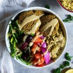 White background with a bowl with falafel, lettuce, veggies, and couscous in it with a tahini drizzle on top.