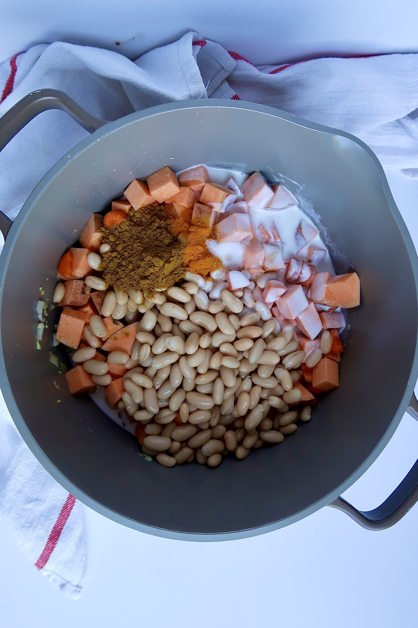 Large pot with diced sweet potato, beans, coconut milk and curry powder inside.