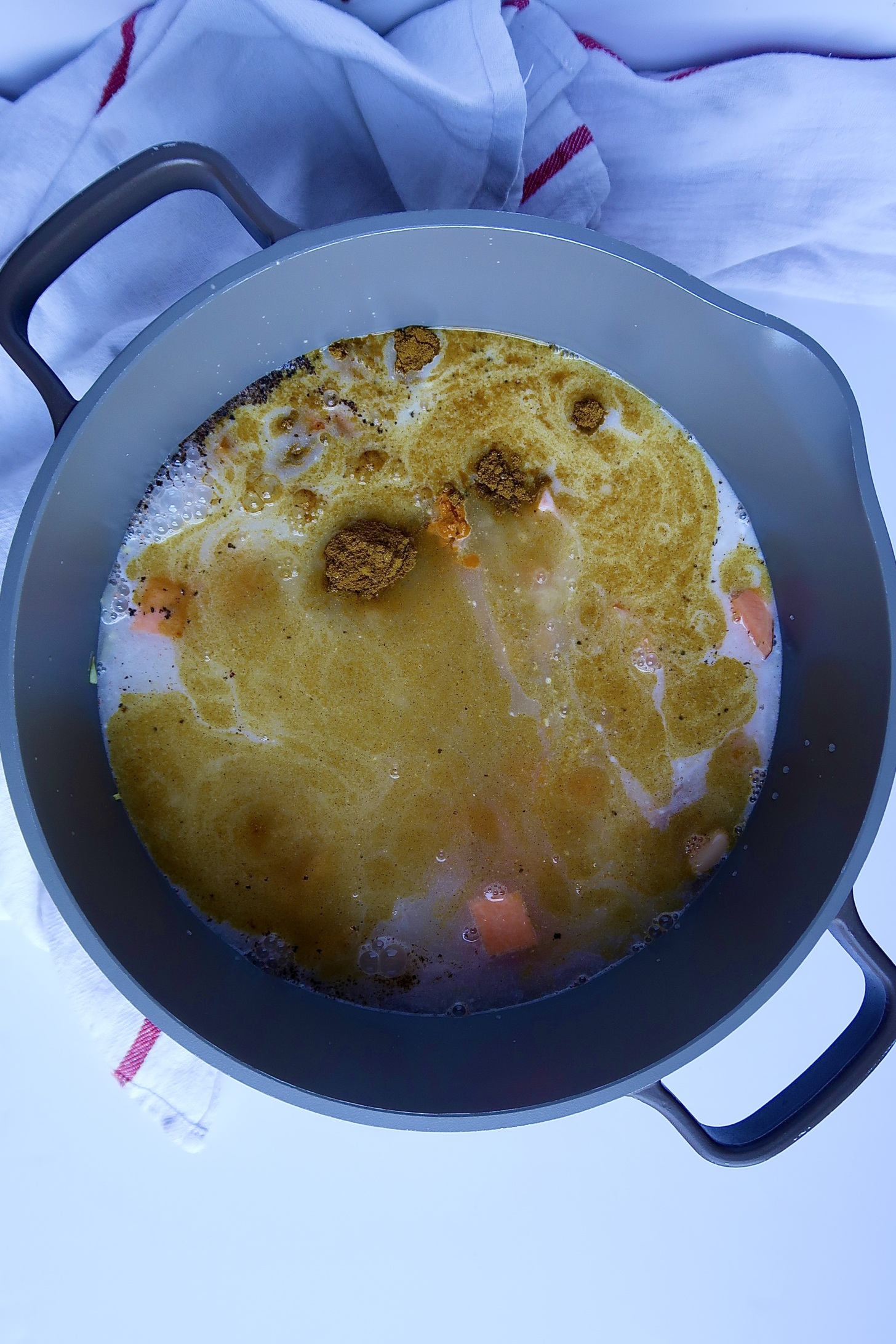 Large pot with coconut milk and spices inside and some sweet potato that's diced.