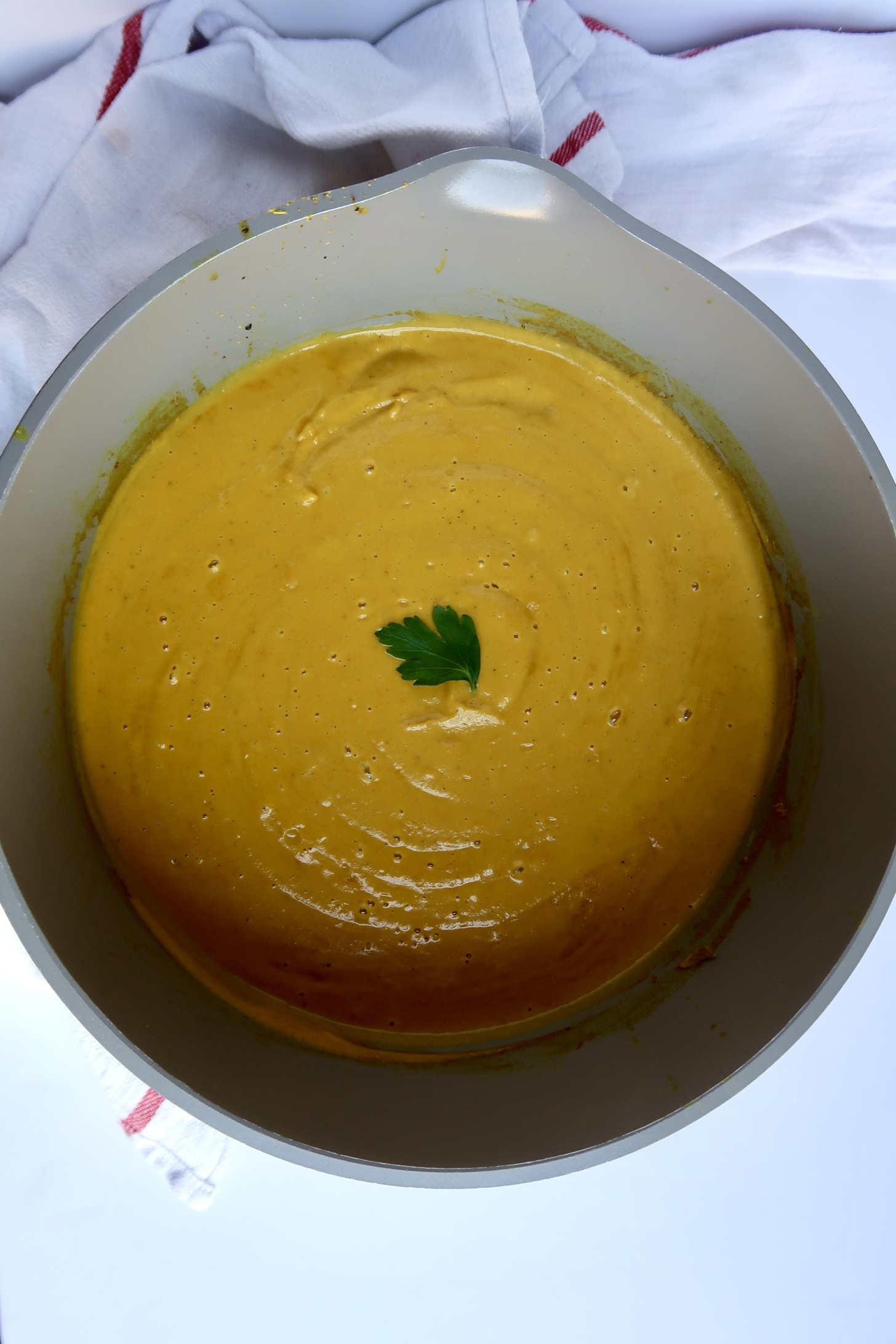 Large pot with a blended, yellow soup inside with cilantro to garnish.