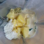 Kale, pineapple, coconut flakes, hemp seeds and soy milk in a smoothie jug.