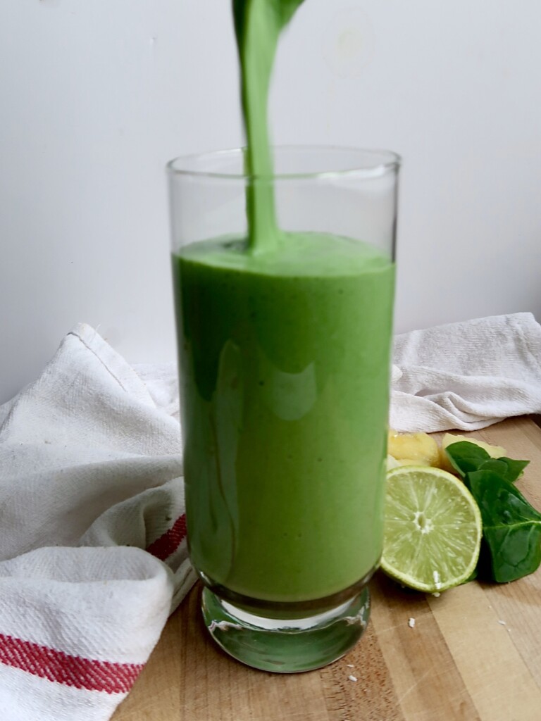 Glass with a green smoothie being poured into it and fresh lime on the side.