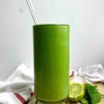 Green smoothie in a glass with a glass straw in it and lime to the side.