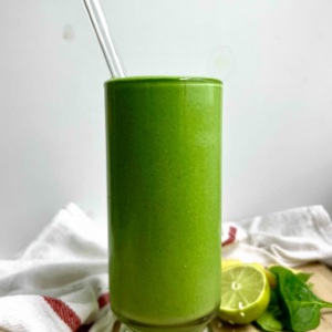 Green smoothie in a glass with a glass straw in it and lime to the side.