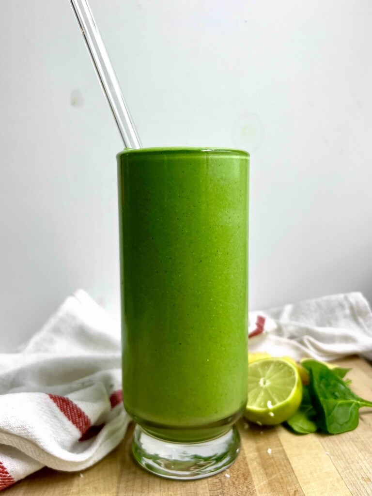 Green smoothie in a glass with a glass straw in it and lime to the side.