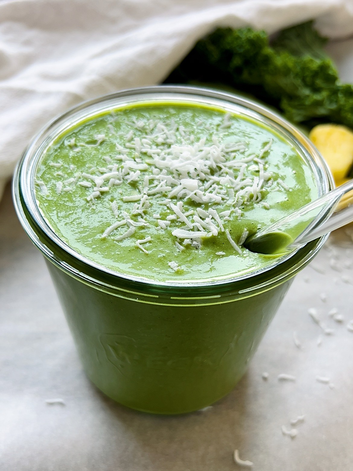 Green smoothie in a mason jar with kale and pineapple on the side.