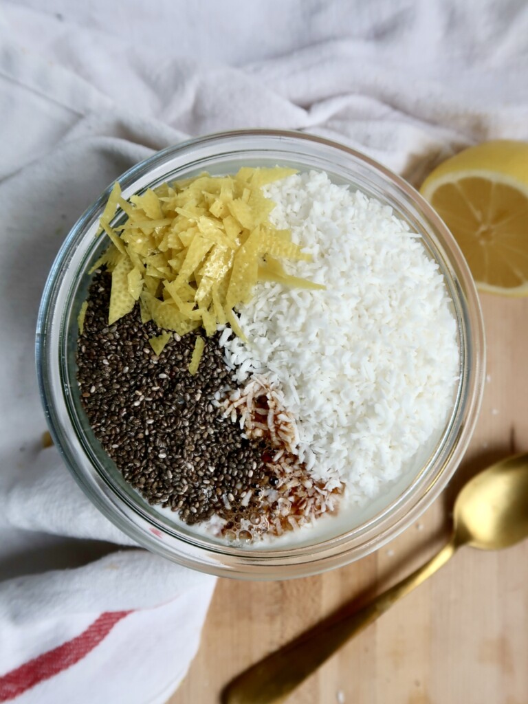 Overhead shot of jar with plant based milk, coconut flakes, lemon zest and chia seeds on top.