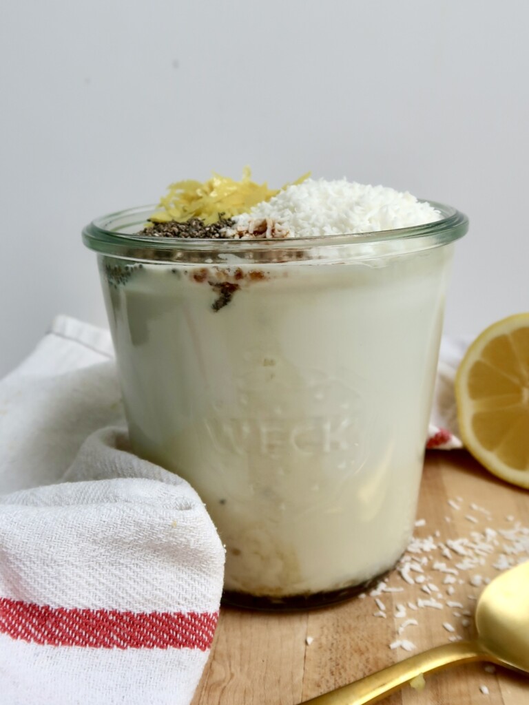 Jar with plant based milk, coconut flakes, lemon zest and chia seeds on top.