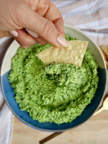 Bowl with edamame dip in it and a hand dipping a corn chip with edamame dip.