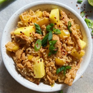 White background and a white bowl with Sweet & Sour Pineapple Soy Curl Stir Fry, with chunks of pineapple and soy curls with parsley on top.