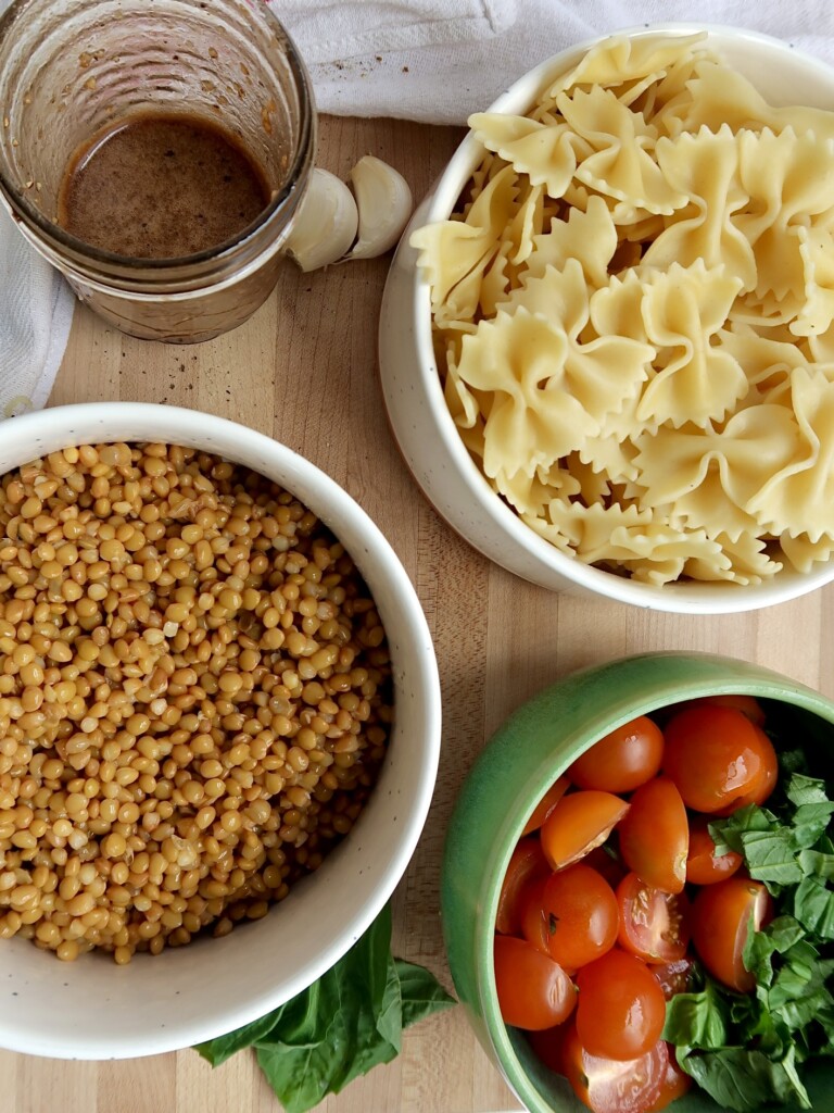 Pasta, lentils, cherry tomatoes, basil, and balsamic dressing on a cutting board.