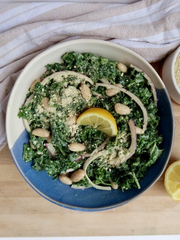 White and blue bowl with kale caesar in it with a lemon on top.