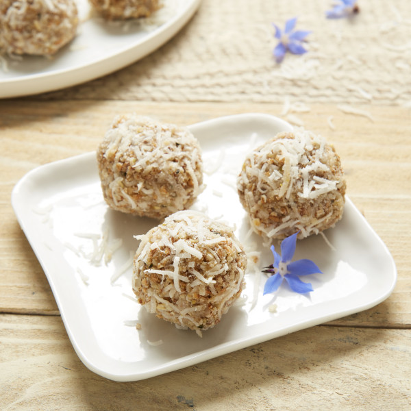 Lemon coconut energy balls on a plate with small purple flowers