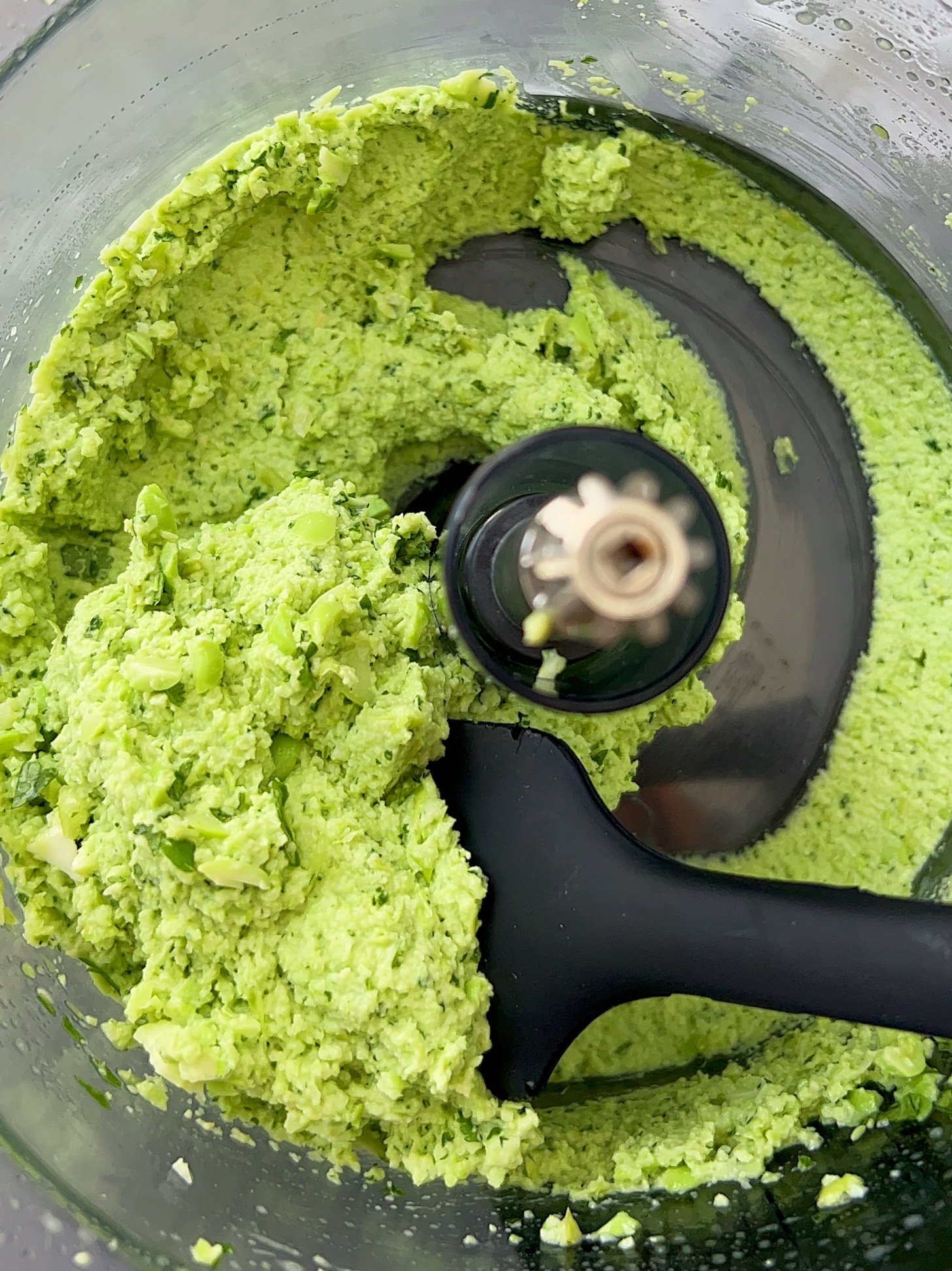 Food processor with cilantro lime dip inside and a spatula scooping some.