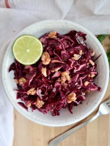 Cabbage salad in a bowl with walnuts and lime.