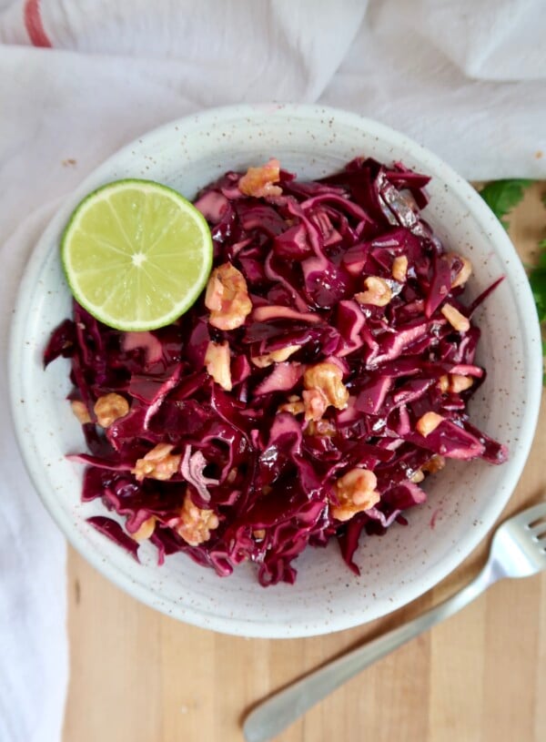 Cabbage salad in a bowl with walnuts and lime.
