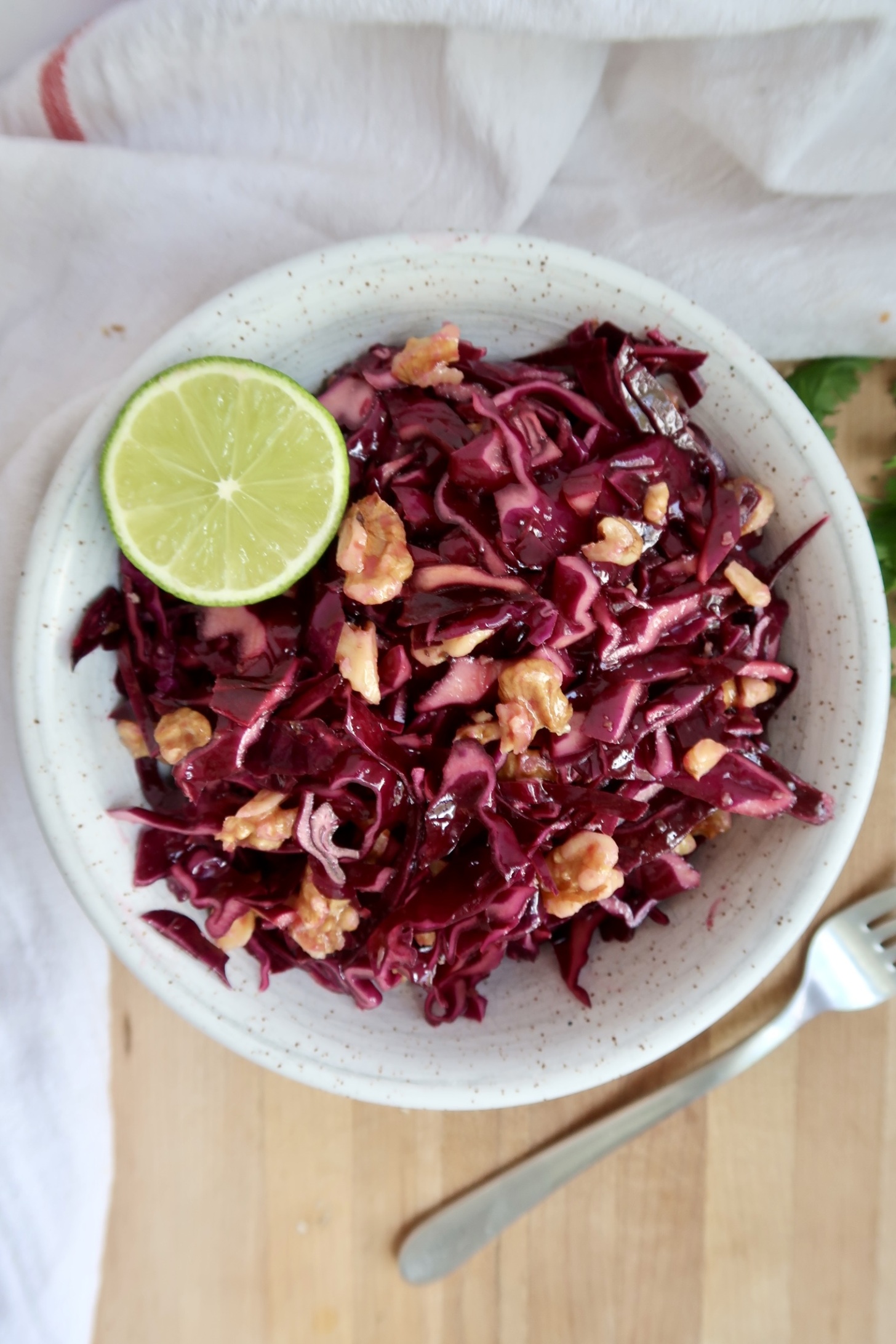 Cabbage salad in a bowl with walnuts and lime.