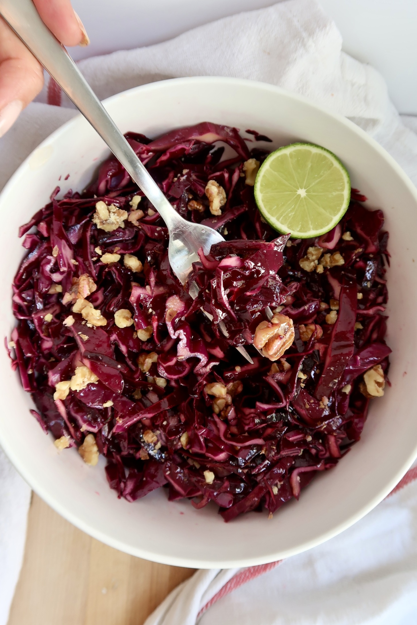Cabbage in a bowl with walnuts and lime and fork taking some.