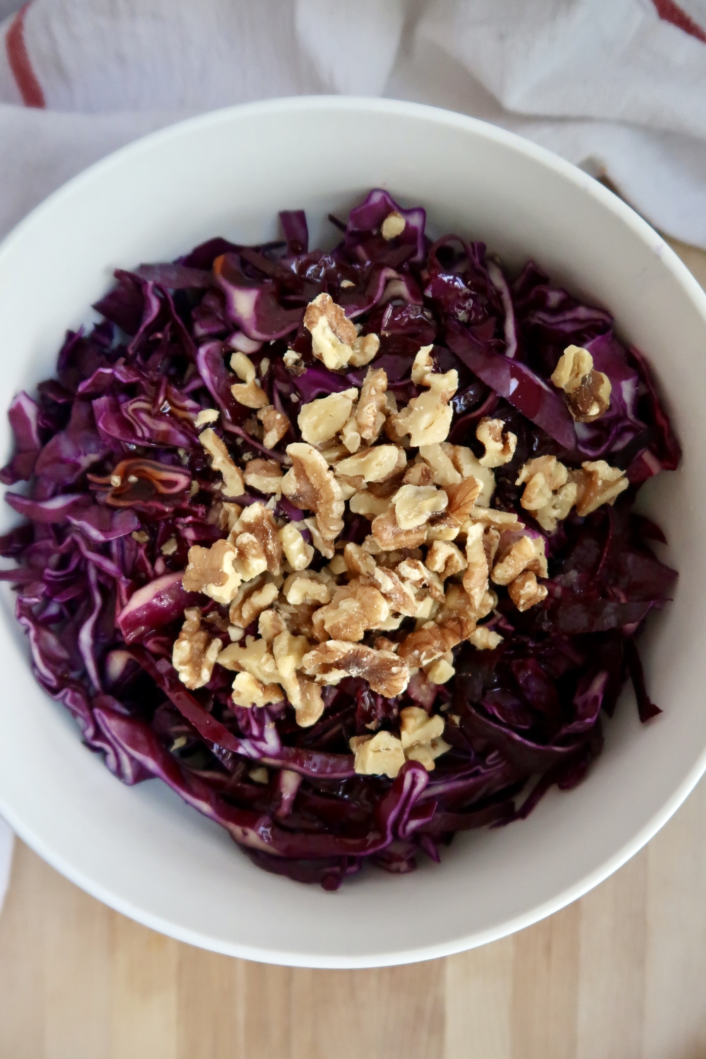 Purple cabbage salad in a bowl wtih walnuts on top.