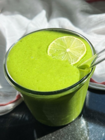 Green smoothie in a jar with lime to garnish and a white cloth in the background.