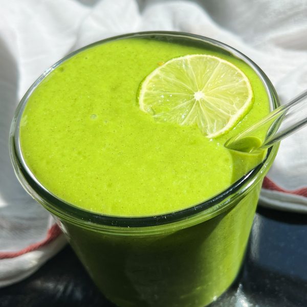 Green smoothie in a jar with lime to garnish and a white cloth in the background.
